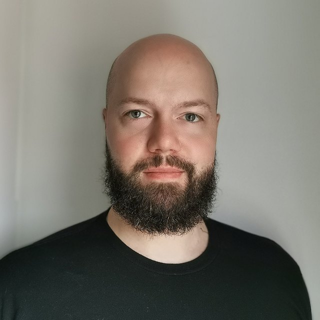 Chris Joubert, shaved head and full beard, in a black shirt, looking at the camera